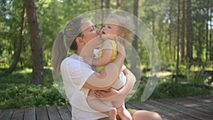 Little cute baby toddler girl blonde with curls on mother's arms. Mother and daughter playing spend time together
