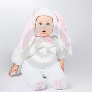 Little cute baby in a white Bunny suit. The child sits on the floor.