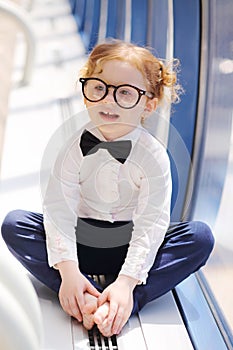 Little cute barefoot girl in glasses sits on floor