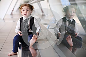 Little cute barefoot girl in tie sits on floor