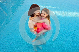 Little cute beautiful girl hugs mom in an exotic pool with turquoise water.