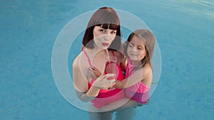 Little cute beautiful girl hugs mom in an exotic pool with turquoise water.