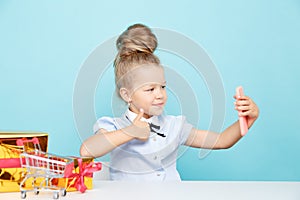 Little cute blogger making selfie on the phone sititng with a lot of presents on the table.