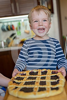 Little cute blond boy with happy smile enjoys baked berry pie with wild berry jam. Concept of happy childhood