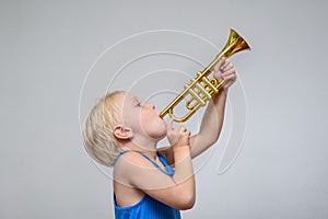 Little cute blond boy playing toy trumpet on light background