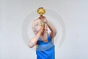 Little cute blond boy playing toy trumpet on light background