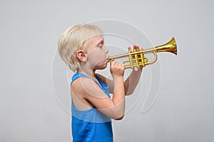 Little cute blond boy playing toy trumpet on light background