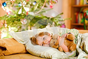 Little cute blond boy sleeping under Christmas tree and dreaming of Santa at home, indoors. Traditional Christian