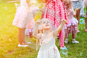 Little cute blond girl in a dress playing with soap bubbles duri