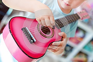 Little cute blond girl having fun learning to play small ukulele guitar at home.Toddler girl playing toy musical