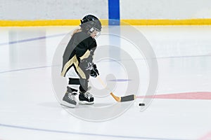 Little cute blond girl plays hockey in full equipment on the stadium