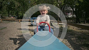Little cute blond girl rides teeter totter at playground