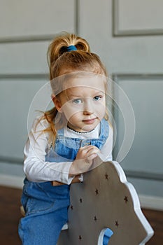 A little cute blonde girl in jeans on a wooden toy rocking horse