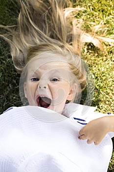 Little cute blonde girl in park laying on green grass smiling, holding white summer hat emotional, lifestyle people