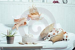 Little cute blonde norwegian girl playing on sofa with pillows, crazy home alone, lifestyle people concept