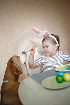 Little cute blue-eyed girl and beagle puppy paint easter eggs