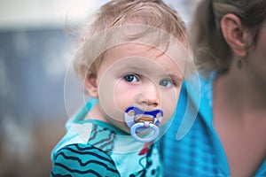 Little cute boy with a baby pacifier in his mouth in his mother`