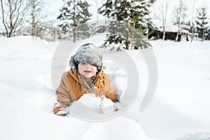 Little cute boy in black hat,orange jacket is lying,playing in snow. Kid walking in beautiful frozen forest,park among