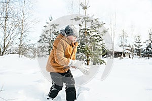 Little cute boy in black hat,orange jacket is lying,playing in snow. Kid walking in beautiful frozen forest,park among