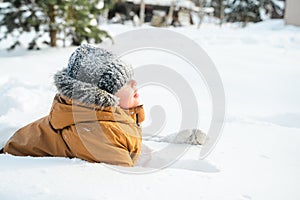 Little cute boy in black hat,orange jacket is lying,playing in snow. Kid walking in beautiful frozen forest,park among