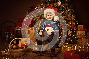 Little Cute Boy in Christmas Decorated Room Interior. Child on vintage wooden Toy Horse. Christmas tree with rustic ornament