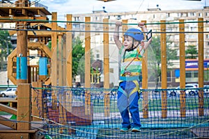 Little cute boy enjoying activity in a climbing adventure park on a summer sunny day. toddler climbing in a rope playground