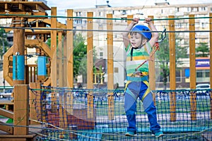 Little cute boy enjoying activity in a climbing adventure park on a summer sunny day. toddler climbing in a rope playground