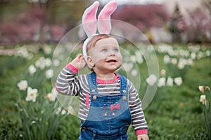 Little cute boy and girl are sitting on the grass near the daffodils. Children in costumes Easter bunnies