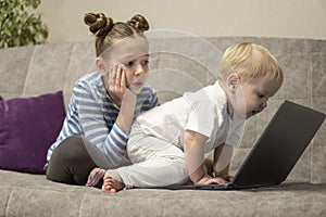 Little cute boy and girl using laptop together, looking at screen, watching cartoons or playing online, sister and brother,