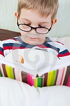 Little cute boy reading book in bed