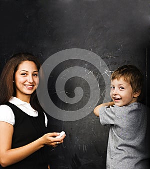 Little cute boy in glasses with young real teacher, classroom studying at blackboard school