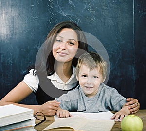 Little cute boy in glasses with young real teacher, classroom studying at blackboard school kido