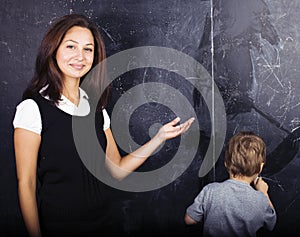 Little cute boy in glasses with young real teacher, classroom studying at blackboard school kido