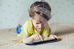 Little cute boy in a green T-shirt playing games on a tablet and watching cartoons. addiction concept