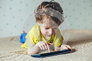 Little cute boy in a green T-shirt playing games on a tablet and watching cartoons. addiction concept