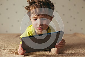 Little cute boy in a green T-shirt playing games on a tablet and watching cartoons. Toddler with tablet.