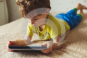 Little cute boy in a green T-shirt playing games on a tablet and watching cartoons. Toddler with tablet.