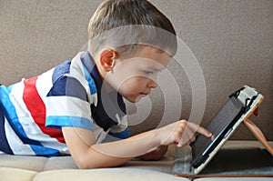 Little cute boy in a green T-shirt playing games on a tablet and watching cartoons. Toddler with tablet.