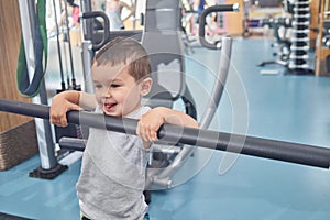 Little cute boy grimacing, holding on metallic crossbar in gym.