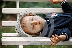 A little cute boy in a hat, lying on a white bench in the garden to rest