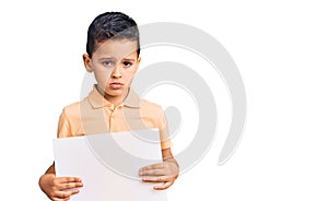 Little cute boy kid holding cardboard banner with blank space thinking attitude and sober expression looking self confident