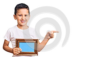 Little cute boy kid holding empty frame smiling happy pointing with hand and finger to the side