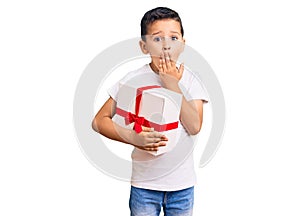 Little cute boy kid holding gift covering mouth with hand, shocked and afraid for mistake