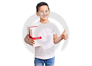 Little cute boy kid holding gift smiling happy and positive, thumb up doing excellent and approval sign