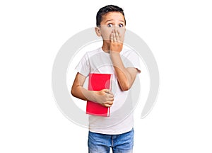 Little cute boy kid reading a book covering mouth with hand, shocked and afraid for mistake