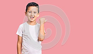 Little cute boy kid wearing casual white tshirt smiling with happy face looking and pointing to the side with thumb up