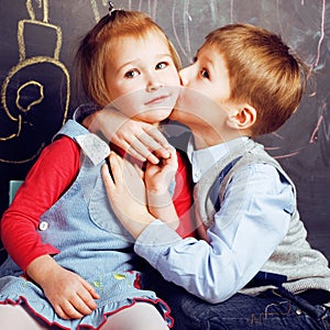 Little cute boy kissing blonde girl in classroom at blackboard, first school love, lifestyle people concept