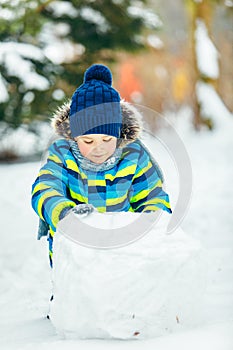 Little cute boy making snowman. rolling big snowball
