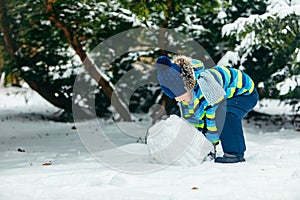 little cute boy making snowman. rolling big snowball