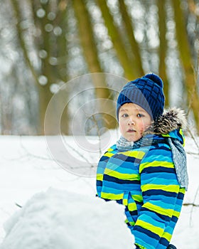 little cute boy making snowman. rolling big snowball